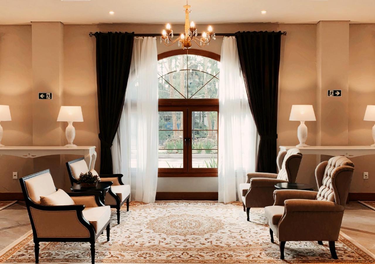 Buona Vitta Gramado Resort & Spa By Gramado Parks エクステリア 写真 The photo shows an elegantly styled living room. There are two armchairs and a sofa arranged comfortably around an intricate area rug. Large windows are adorned with sheer white curtains and dark curtains, allowing natural light to fill the space. A 