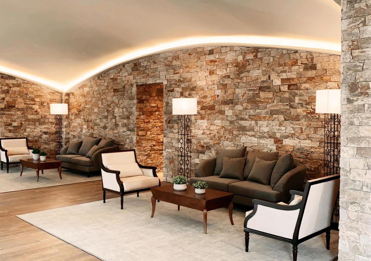 Buona Vitta Gramado Resort & Spa By Gramado Parks エクステリア 写真 The photo shows a stylish and modern lounge area. The walls are made of natural stone, creating a warm and inviting atmosphere. There are two comfortable sofas in a muted gray color arranged around a wooden coffee table. Flanking the sofas are elegan