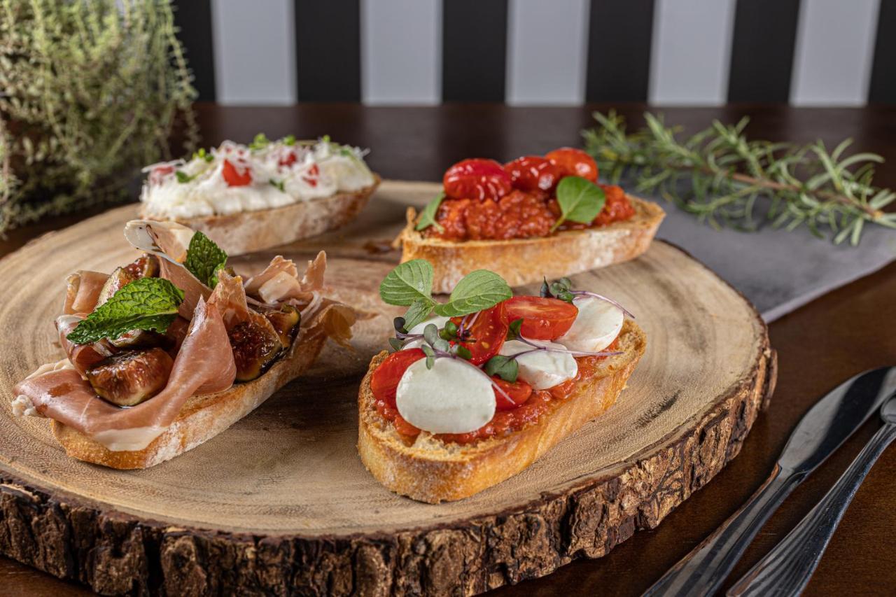 Buona Vitta Gramado Resort & Spa By Gramado Parks エクステリア 写真 The photo displays a wooden serving platter featuring four different types of bruschetta. Each piece of bruschetta is topped with various ingredients:

1. The top left has a creamy spread, possibly cheese or ricotta, garnished with fresh herbs and sm