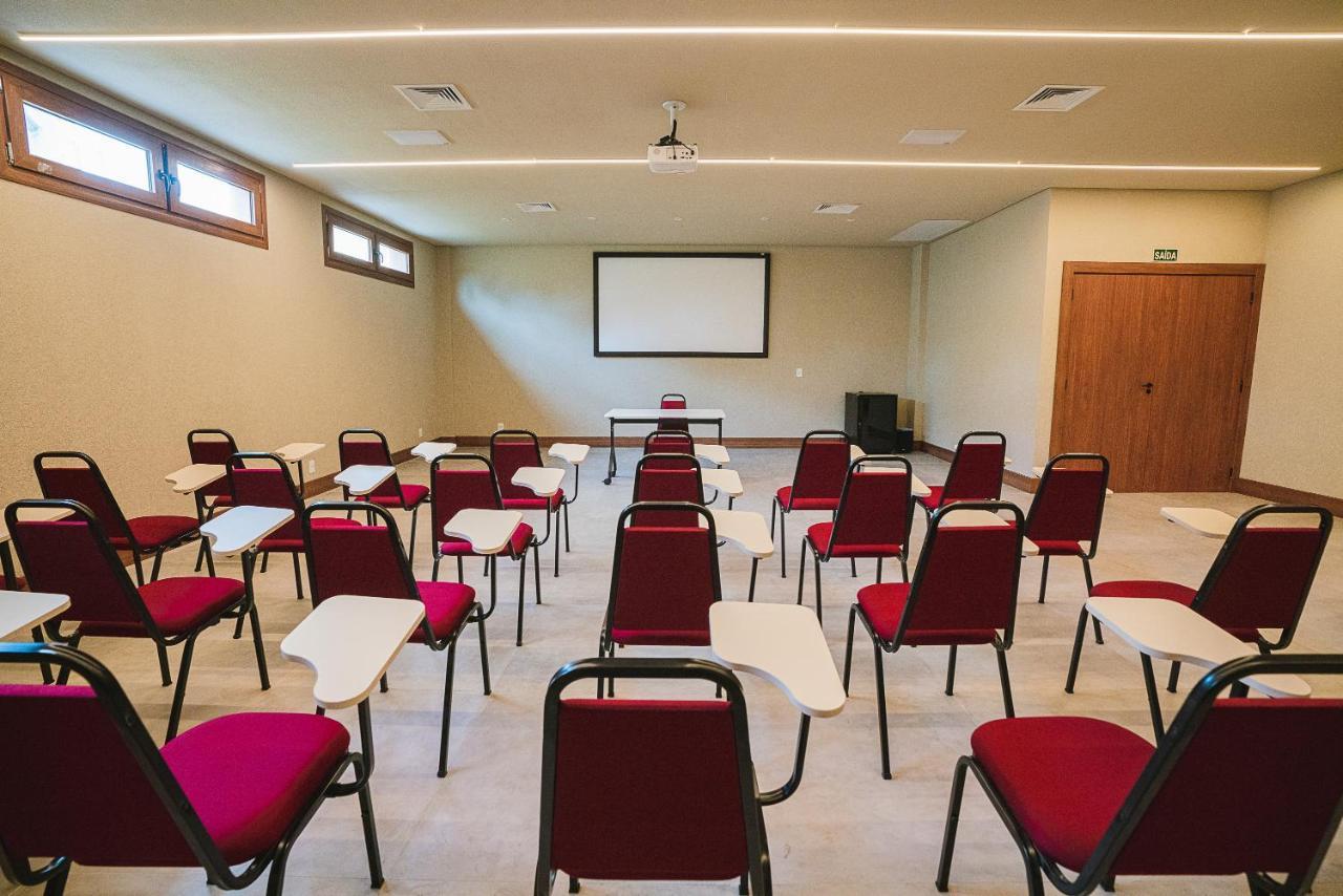 Buona Vitta Gramado Resort & Spa By Gramado Parks エクステリア 写真 The photo shows a classroom or meeting room set up for a presentation or lecture. It features several rows of red chairs, each with a small writing surface attached. There is a blank screen mounted on the wall at the front of the room, likely for dis