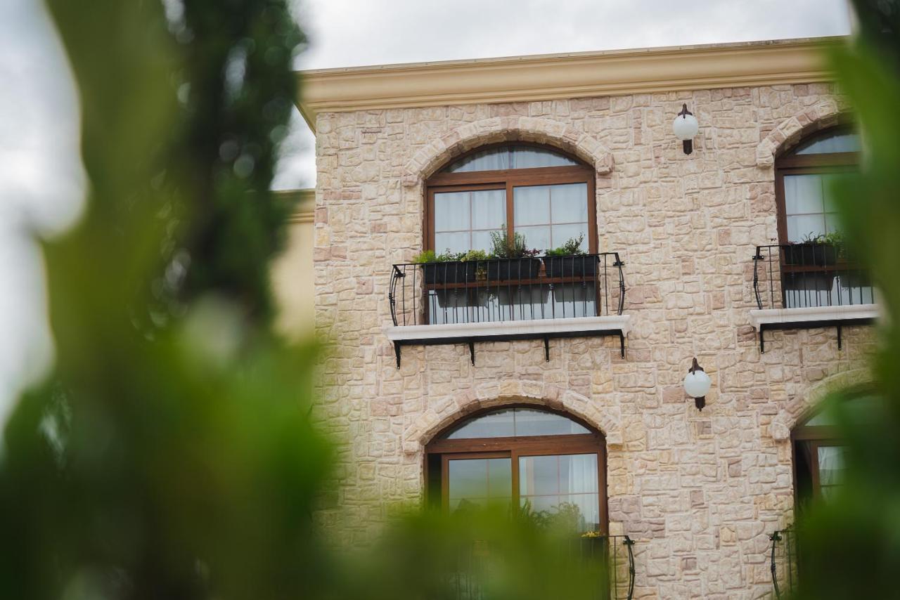 Buona Vitta Gramado Resort & Spa By Gramado Parks エクステリア 写真 The photo depicts a stone building with a textured exterior. It features several windows with wooden frames. Each window has a small balcony adorned with decorative plants. There are also wall-mounted light fixtures flanking the windows. In the foreg