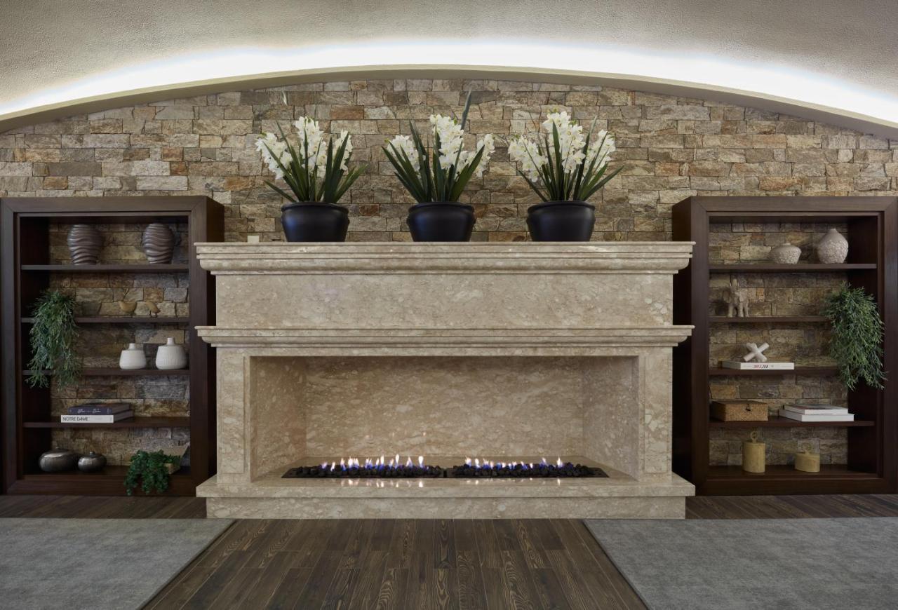 Buona Vitta Gramado Resort & Spa By Gramado Parks エクステリア 写真 The photo shows a modern fireplace design built into a wall with a textured stone background. The fireplace is made of a light-colored stone and features a long, narrow gas flame visible at the bottom. Above the fireplace, there are two large potted 