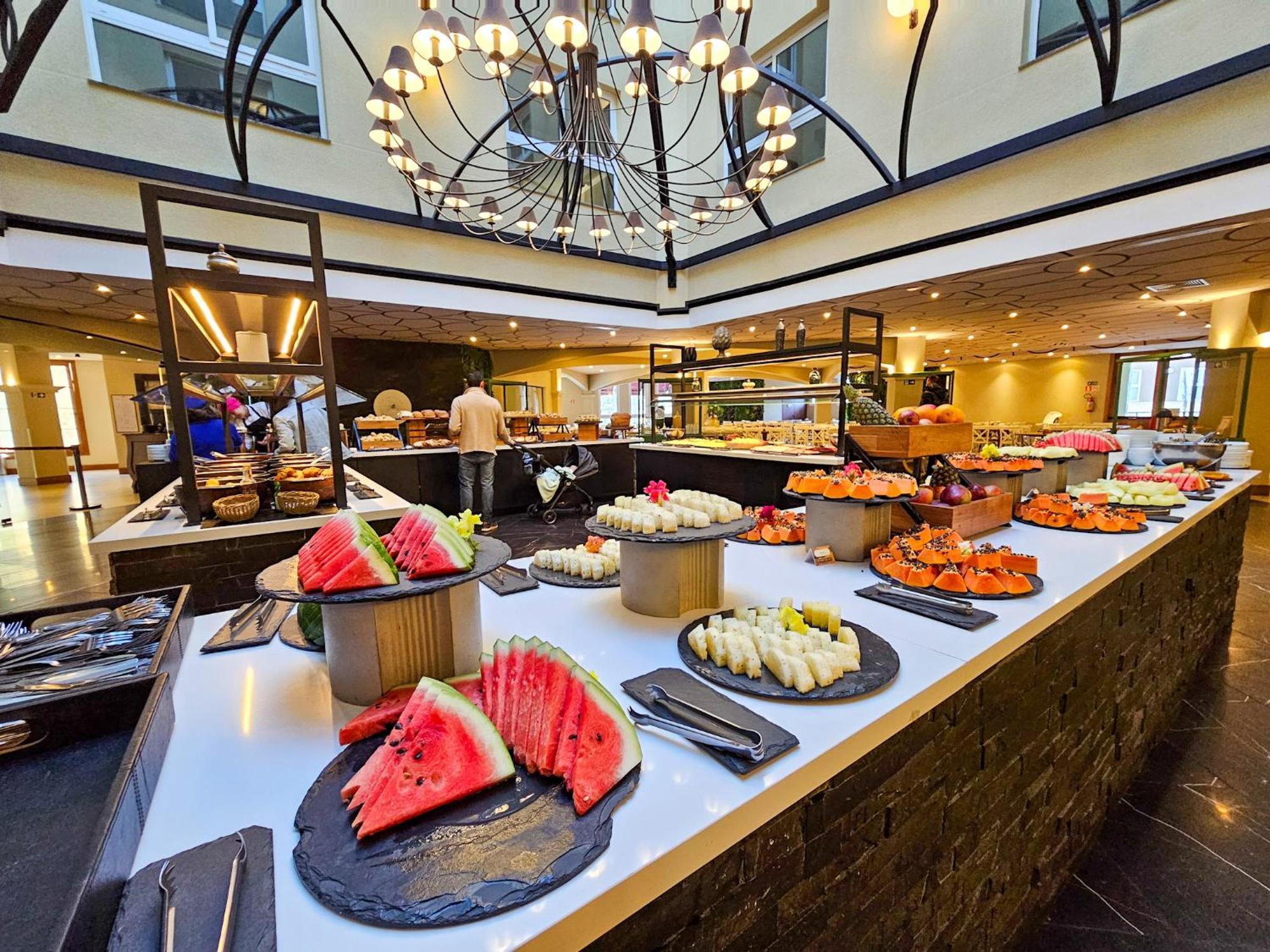 Buona Vitta Gramado Resort & Spa By Gramado Parks エクステリア 写真 The photo depicts a lavish buffet setup in a dining area. In the foreground, there are several platters featuring an assortment of colorful food items, primarily fruits like watermelon and various types of sushi or rolls. The buffet table is elegantl