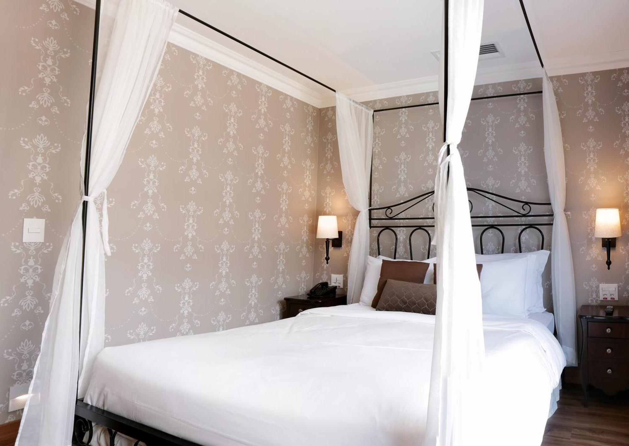 Buona Vitta Gramado Resort & Spa By Gramado Parks エクステリア 写真 The photo shows a elegantly decorated bedroom featuring a four-poster bed with white drapes. The bed is made with white linens and has some brown accent pillows. The walls are adorned with a subtle floral pattern, and there are two bedside lamps prov