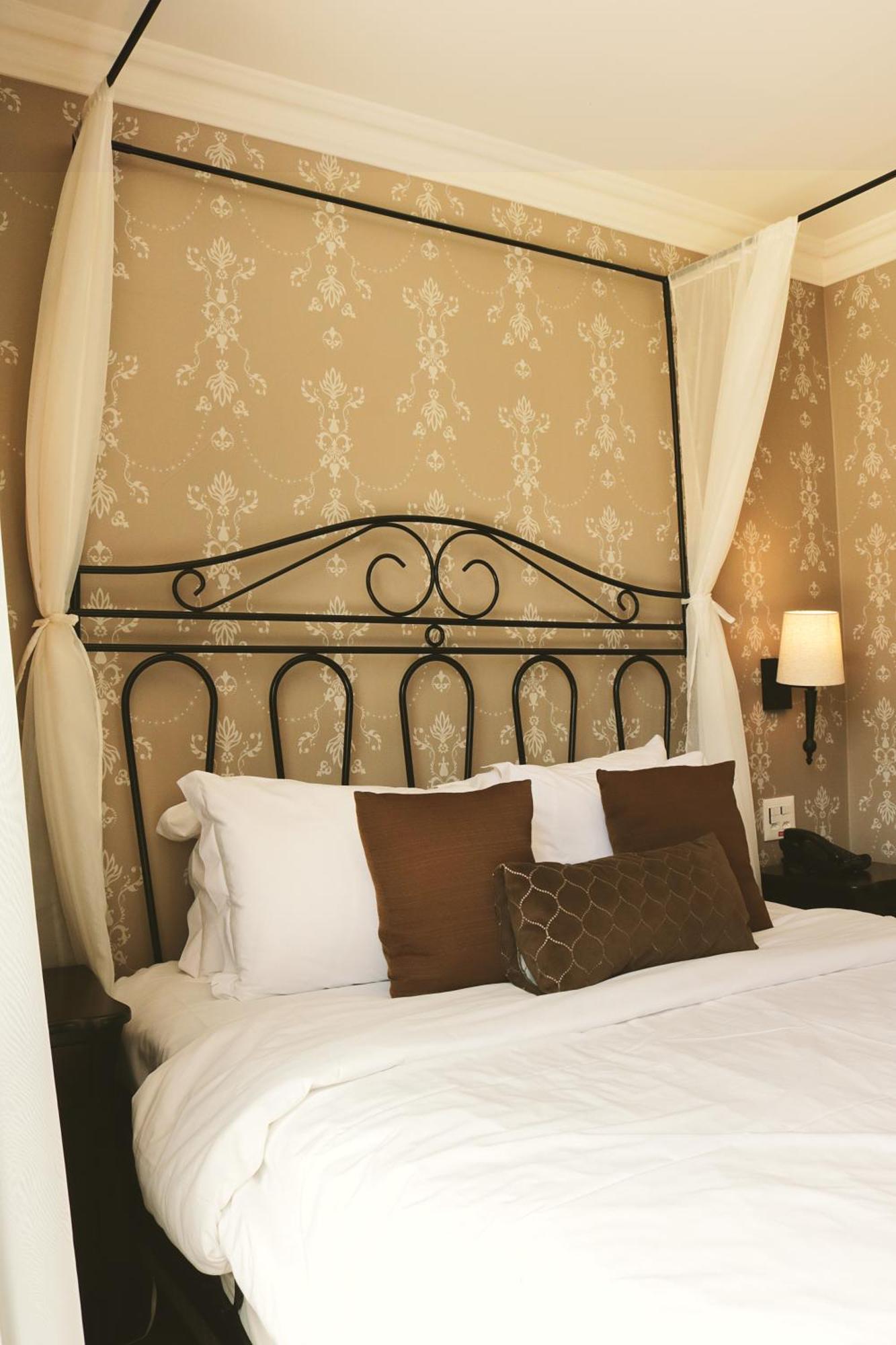 Buona Vitta Gramado Resort & Spa By Gramado Parks エクステリア 写真 The photo shows a cozy bedroom setup featuring a decorative metal bed frame with a scroll design as the headboard. The bed is adorned with several white pillows and two brown decorative cushions. The wall behind the bed is covered with a light-colore