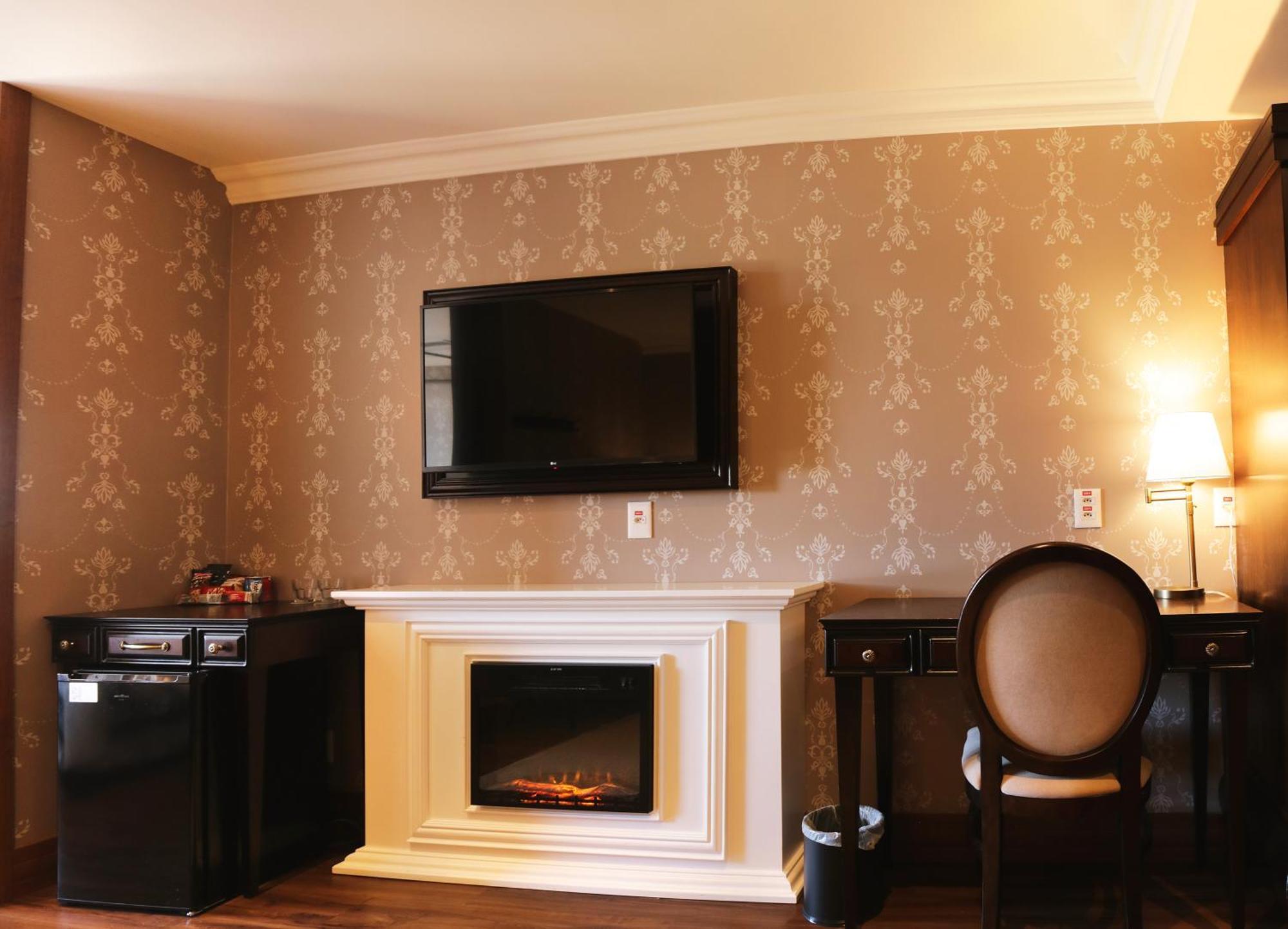 Buona Vitta Gramado Resort & Spa By Gramado Parks エクステリア 写真 The photo shows a cozy room featuring a decorative wall with a subtle pattern. On one side, there is a modern flat-screen television mounted on the wall. Below it, there is a stylish electric fireplace framed in white. Adjacent to the fireplace is a 