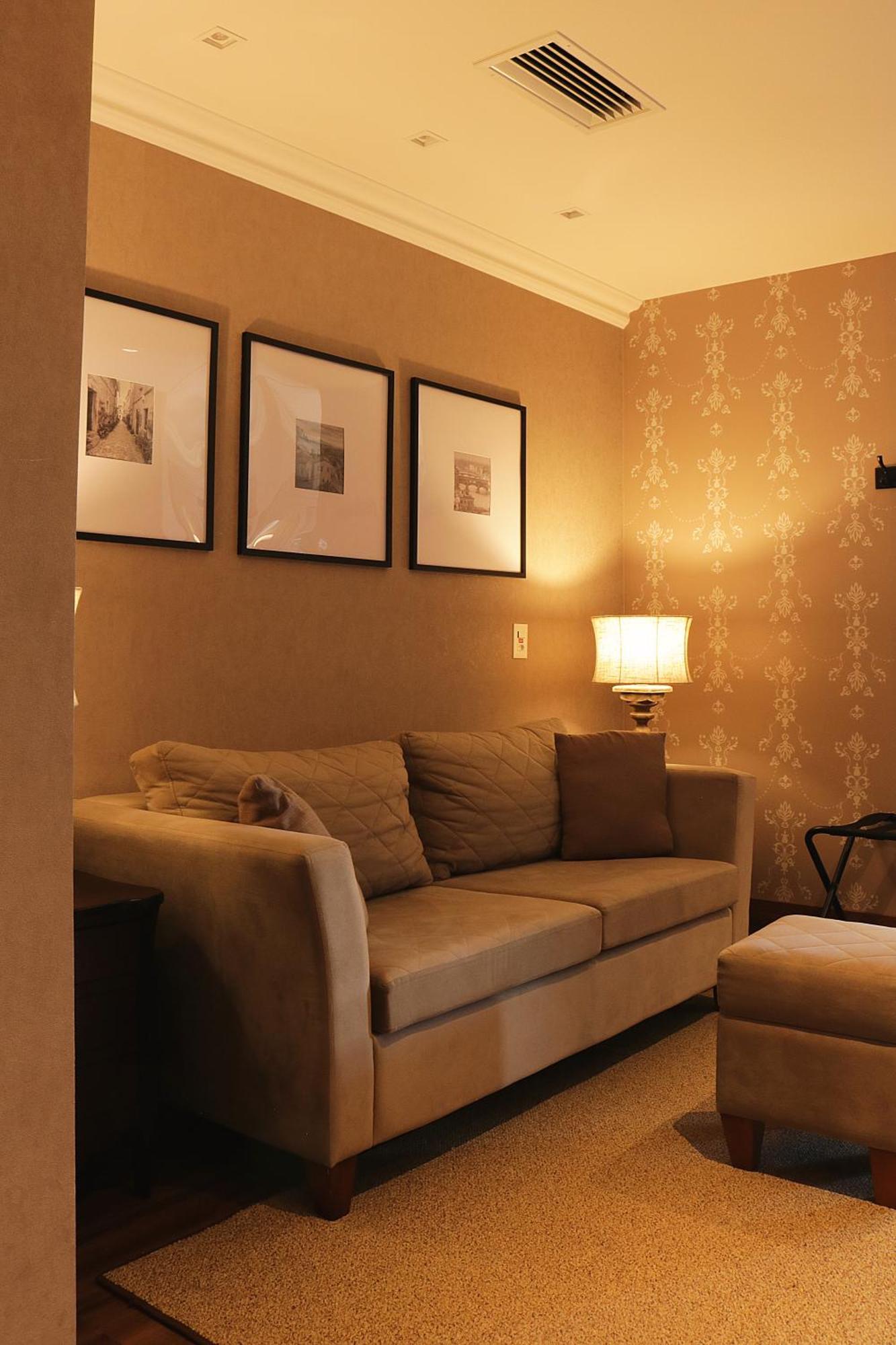 Buona Vitta Gramado Resort & Spa By Gramado Parks エクステリア 写真 The photo shows a cozy living room setting. There is a light-colored sofa adorned with several cushions, positioned against a wall that has a subtle pattern. Above the sofa, there are three framed artworks or photographs hanging on the wall. To the s