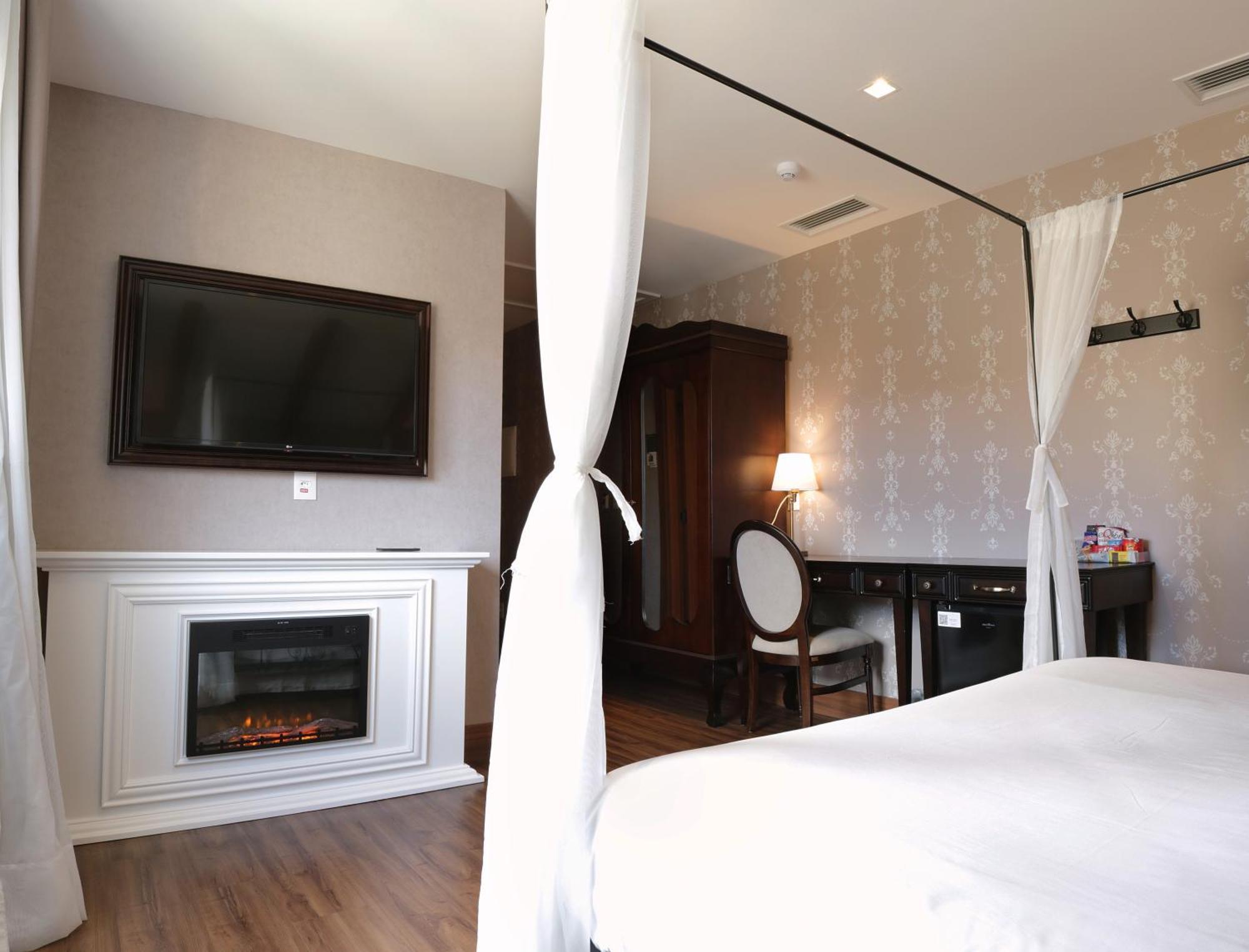Buona Vitta Gramado Resort & Spa By Gramado Parks エクステリア 写真 The photo shows a cozy hotel room with elegant decor. There is a white bed with a canopy, and a modern television mounted on the wall across from it. To the side, a fireplace is built into a white mantel, adding a warm touch to the space. There's a w